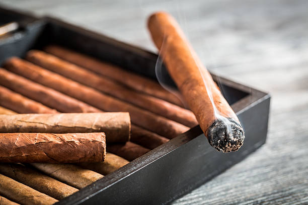 Burning cigar with smoke on wooden humidor.